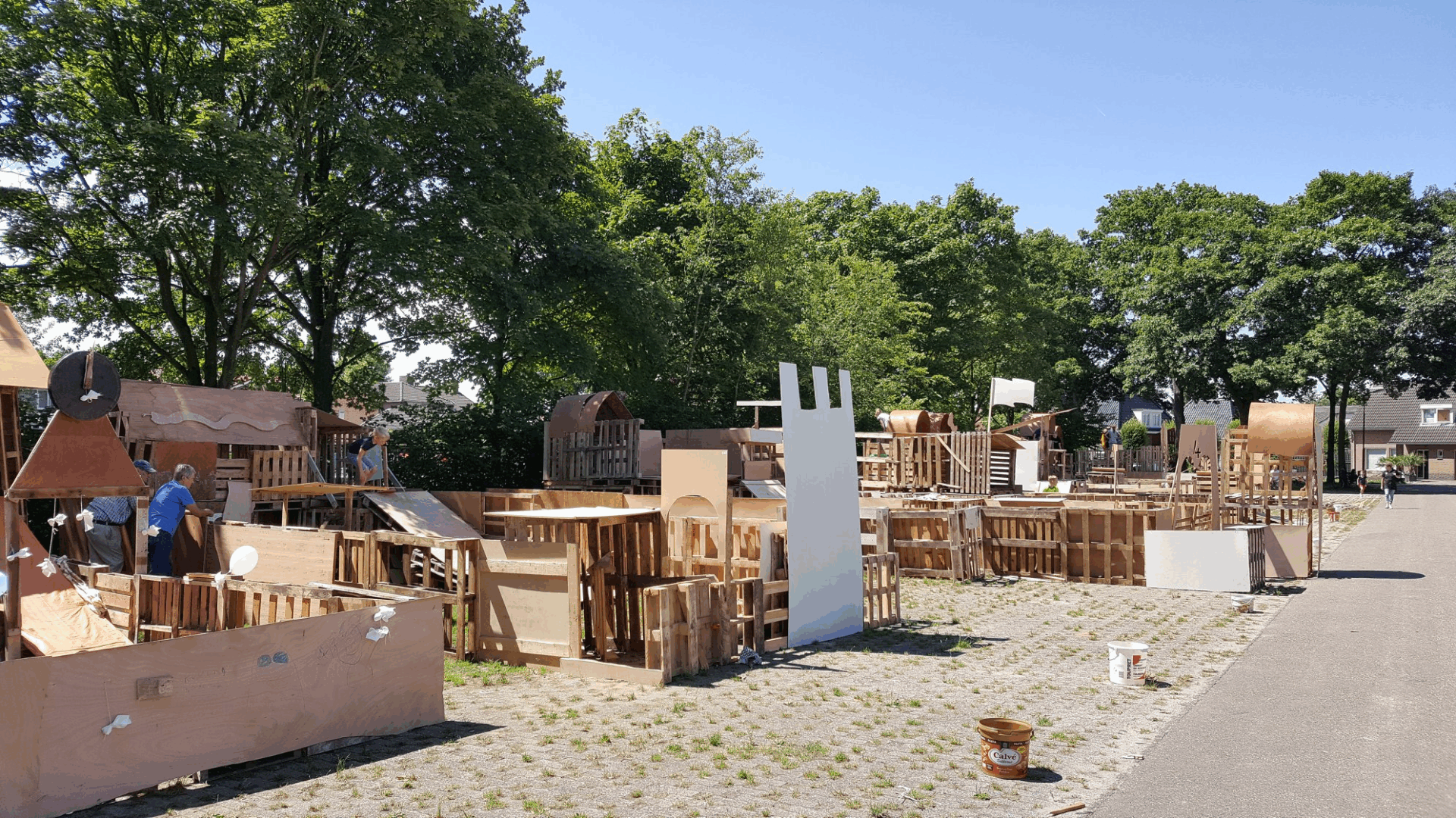 Overzicht van veel houten bouwwerken met 2 begeleiders er bij en 1 kind die van de glijbaan af gaat.